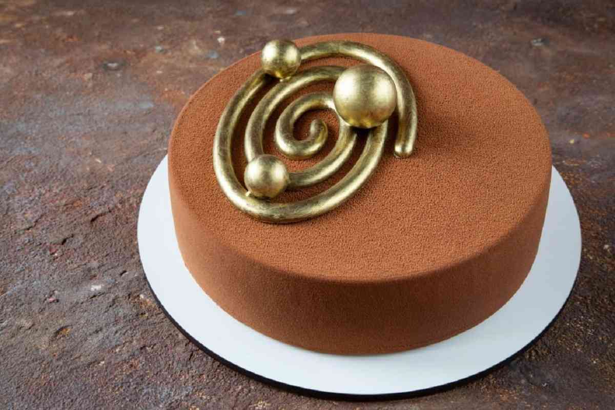 A modern chocolate cake adorned with glossy ganache and edible gold.